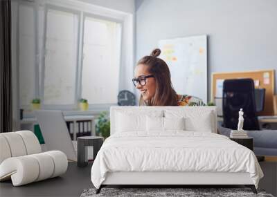 Cheerful attractive young female graphic designer smiling and working at her desk in modern office Wall mural