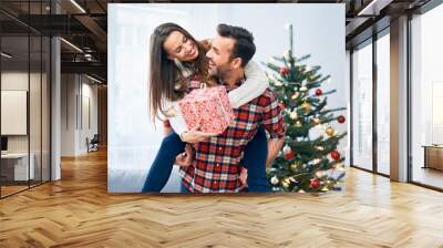 Cheerful couple holding present and goofing around in christmas decorated living room Wall mural