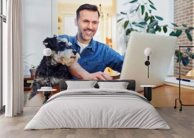 Cheerful man using laptop at home with dog on lap looking on a screen Wall mural