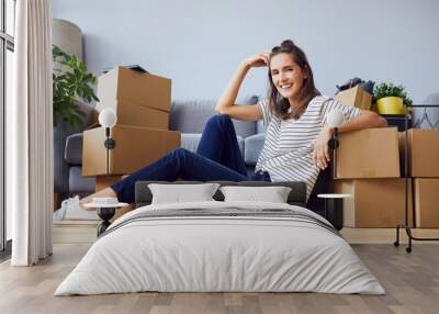 Cheerful young woman sitting in new apartment leaning on boxes after moving in Wall mural