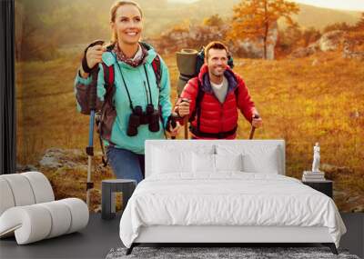 Couple hiking during autumn vacation with sticks and backpacks Wall mural