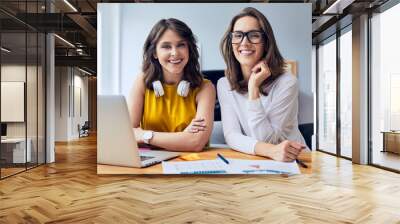 Couple of gorgeous young businesswomen smiling and staring straight at camera while working in office Wall mural