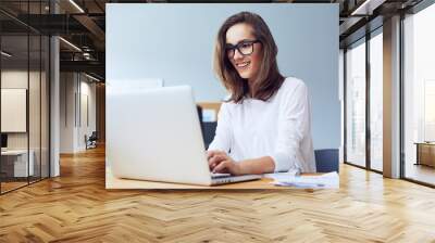 Front view of attractive lady working on laptop and smiling in modern home office Wall mural