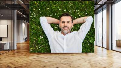 Handsome adult man lying down on grass with daisies Wall mural