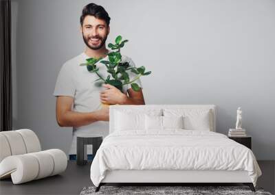 Handsome smiling millennial man holding plant isolated on grey background Wall mural