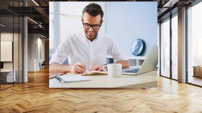 Happy man working from home office doing notes sitting at desk Wall mural