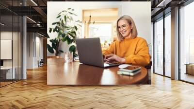 Happy mature woman using laptop while working remotely from home in living room Wall mural