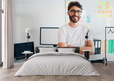 Happy young man sitting on desk in startup office Wall mural