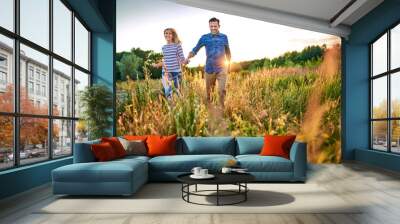 Joyful couple running through meadow on sunny summer day Wall mural