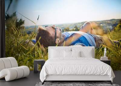 Man lying in grass on hiking trip in the mountains Wall mural