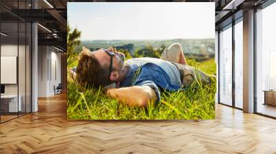 Man lying on grass enjoying peaceful sunny day Wall mural