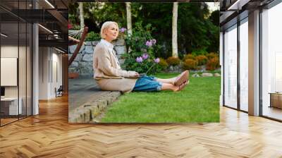 Mature woman using laptop sitting outside her home at backyard patio Wall mural