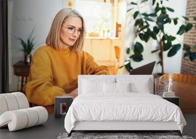 Portrait of adult woman using mobile phone while sitting in living room with laptop Wall mural