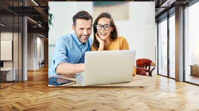 portrait of cheerful couple using laptop together while sitting in cafe Wall mural