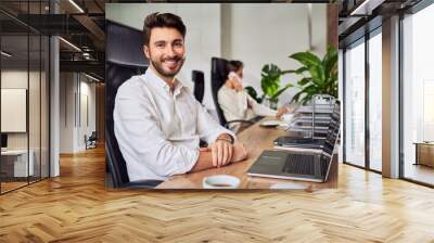 Portrait of handsome young businessman sitting at work in office looking at camera Wall mural