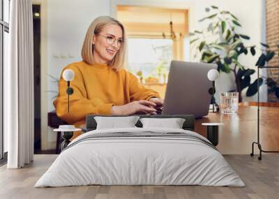 Portrait of middle aged woman sitting at dinning with laptop working at home Wall mural