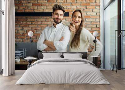 Portrait of successful couple standing at small office. Happy new business partners posing together Wall mural