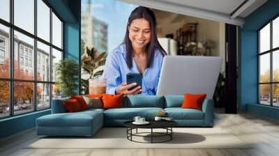 Smiling businesswoman using cellphone and laptop while in cafe Wall mural