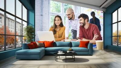 Students looking at laptop while studying together in modern classroom. Startup entrepreneurs brainstorming during meeting Wall mural