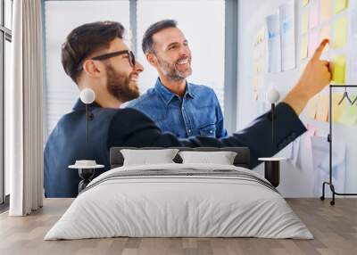 Two coworkers looking at office wall with post it notes talking and brainstorming Wall mural