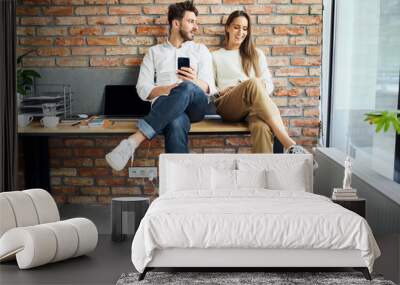 Two happy businesspeople sitting on desk at modern startup office Wall mural