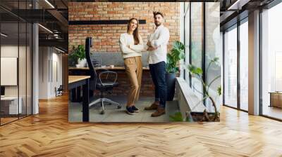 Two small business partners standing together posing in modern office Wall mural