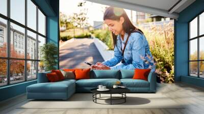 Woman using phone siting outdoors in city Wall mural