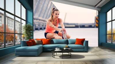 Young athletic woman stretching before running exercise Wall mural