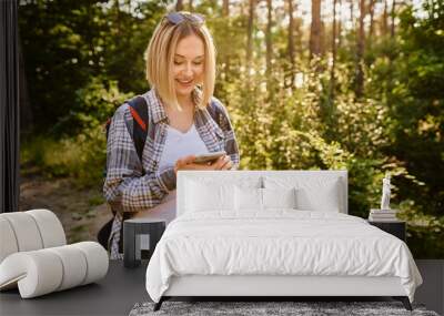 Young woman using mobile phone while walking in the woods during summer hike Wall mural