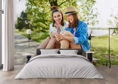 Young women sitting on longboard using phone and drinking lemonade Wall mural