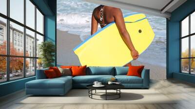 Young woman carrying her body board. Wall mural