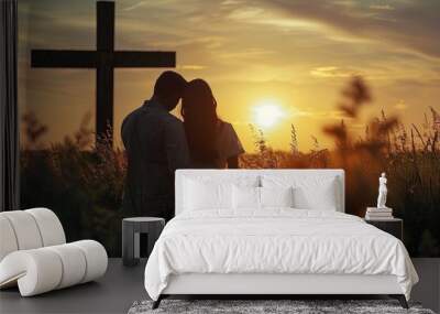 Couple praying God together in field in front of cross at sunset. Wall mural