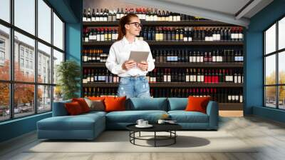 Female retail manager in liquor store with shelves of wine bottles in background. Wall mural