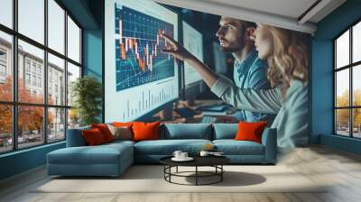 Man and woman coworkers in office dressed in suit sitting at desk with computer looking at data chart graph on monitor analyzing Wall mural