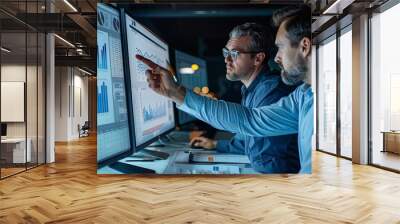 Two people data analysts men in office working together at laptop looking at chart poiting at monitor Wall mural