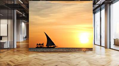 A traditional dhow boat sails through a calm and beautiful blue ocean silhouetted by the setting sun in Zanzibar, Tanzania, Africa. Wall mural