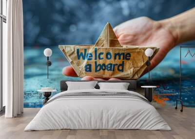 Hand presenting a paper boat with the message Welcome aboard against a blue background, symbolizing new beginnings and joining a team or company Wall mural