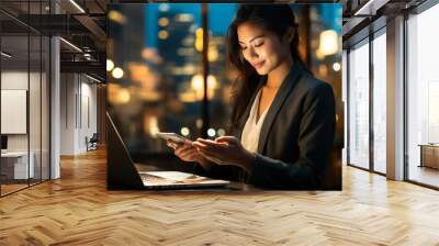 Young happy busy Asian business woman executive using laptop mobile cell phone tech at night in dark office. Professional businesswoman holding smartphone, working on cellphone Wall mural