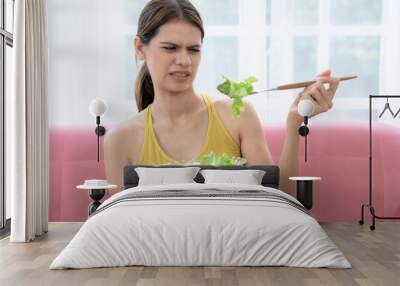 Unhappy young Caucasian woman does not want to eat vegetables and does not like the bitter taste of vegetables. Wall mural