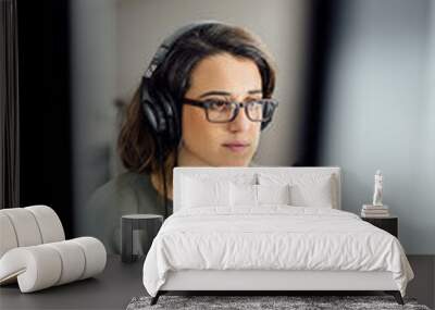 Female adult with casual clothing, headphones and glasses, working on a computer. Busy Freelance worker, sitting at work or home, reading email from client, long hours of work concept.  Wall mural