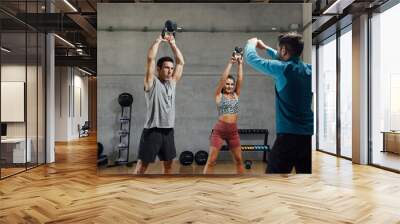 Fitness instructor giving kettle bell class in dark shadow gym Wall mural