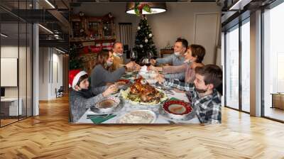 Happy family members wearing surgical masks toasting at the Christmas Thanksgiving table at home in the year of the Covid-19 Pandemic. New rules, new health regulations. Wall mural