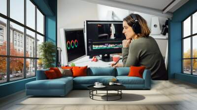 Profile view of Female designer sitting, editing video on a computer at her workplace. Modern business woman working concentrated in video design with a pen tablet in a studio. Freelance worker. Wall mural