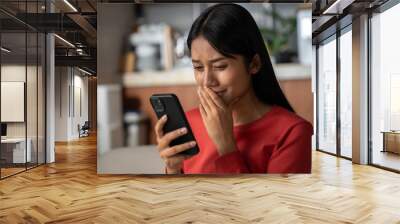 Beautiful asian woman looking to phone and crying. She was shocked with the bad news she received. Wall mural