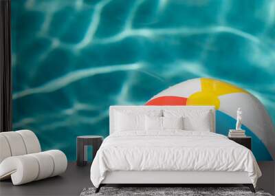 Red, white, yellow and blue beach ball floating on blue water in a pool on a hot summer day Wall mural