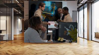 Caucasian male artist designer with dreadlocks and glasses draws on a tablet a 3D model for a computer game in the office of a project development studio.  Wall mural