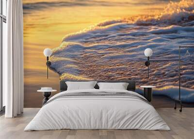 Golden sunset light illuminates foamy wave on a sandy beach. Wall mural