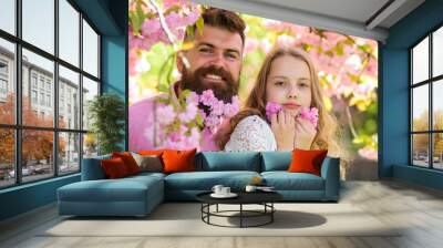 Childhood concept. Father and daughter on happy faces play with flowers, sakura background. Girl with dad near sakura flowers on spring day. Child and man with tender pink flowers in beard. Wall mural