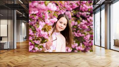 Girl tourist posing near sakura. Tender bloom. Child on pink flowers of sakura tree background. Girl enjoying cherry blossom or sakura. Cute child enjoy warm spring day. Aromatic blossom concept Wall mural