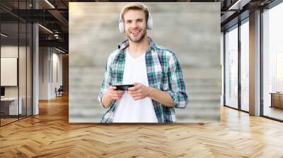 Go wireless with technology. Happy man play music in smartphone. Handsome guy wear headphones. New technology. Mobile technology. Modern life. Fine technology only for your ears Wall mural